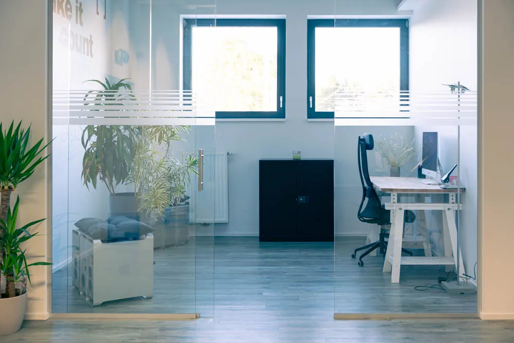 Un bureau derrière une cloison vitrée, plantes et lumière du jour